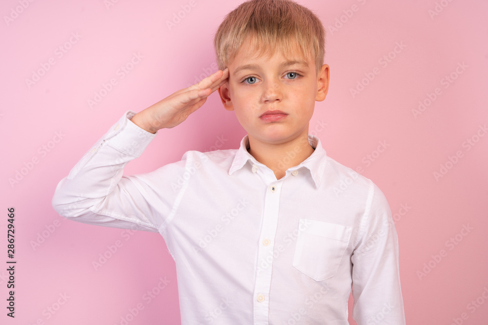Portrait of handsome schoolboy. Young white haired guy with facial hair in white casual shirt saluting with hand at forehead. Portrait of handsome schoolboy. Young white haired guy with facial hair in white casual shirt saluting with hand at forehead.
