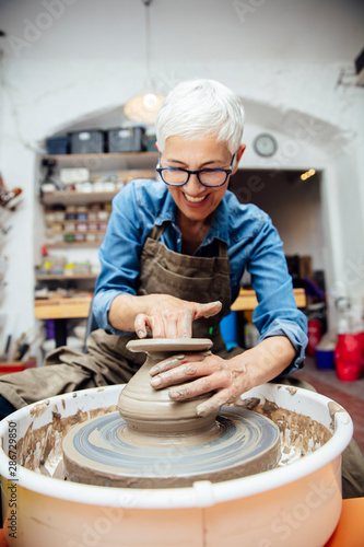 Senior female potter working on pottery wheel while sitting  in her workshop © BGStock72