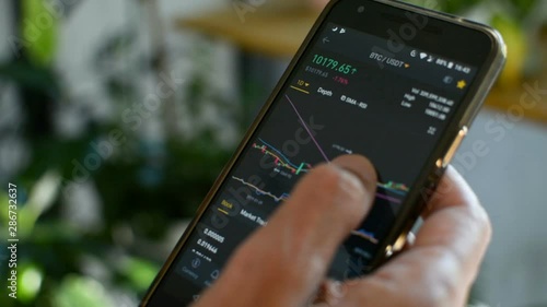 Businessman is checking Bitcoin price chart on crypto exchange on amobile phone screen. Cryptocurrency future price prediction concept.