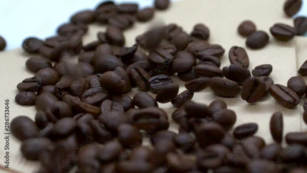 Brown, Roasted coffee beans, falling on a white, spinning on a paper, on a table. Brown, Roasted coffee beans, falling on a white, spinning on a paper, on a table.