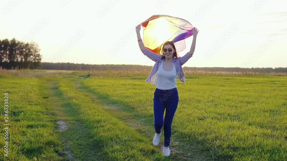 young woman holding an LGBT flag runs across a field at sunset slow mo young woman holding an LGBT flag runs across a field at sunset slow mo