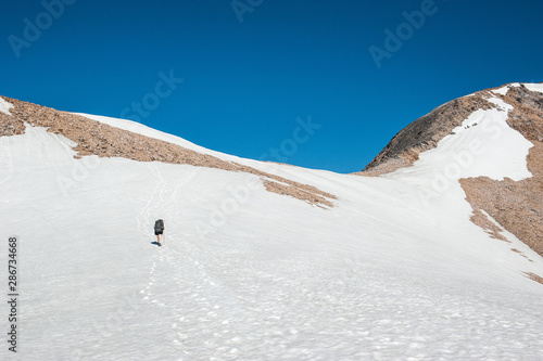 A young woman with backpack and pole hiking on iceberg and snow and enjoying the views of the Andes mountains and lake near Refugio Italia Manfredo Segré (Laguna Negra) in Patagonia, Argentina. Winter photo