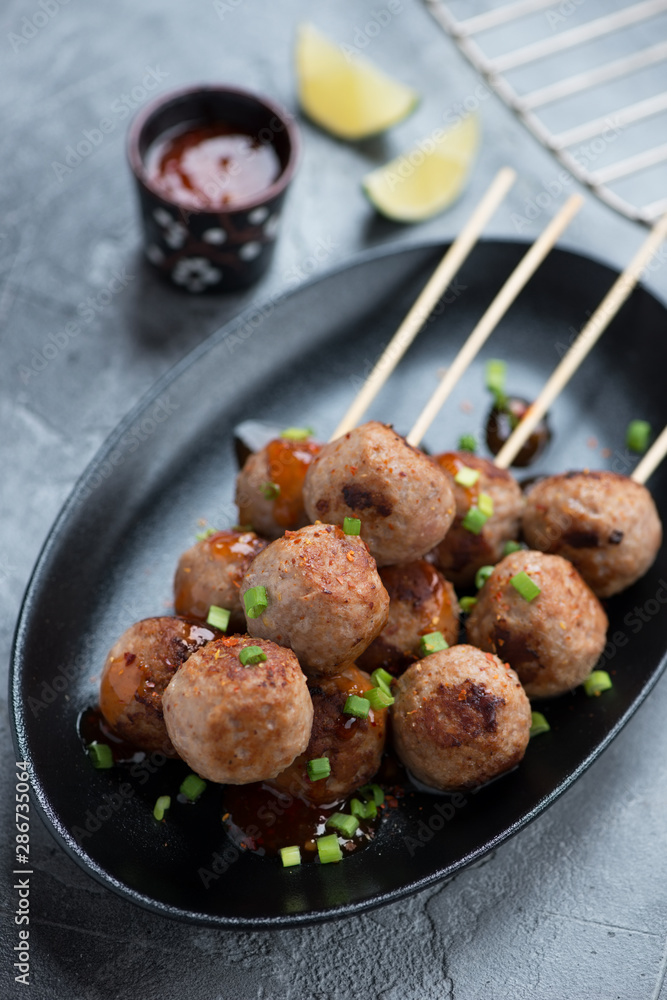 Black plate with nem nuong or fried vietnamese pork meatballs on skewers, closeup, vertical shot Black plate with nem nuong or fried vietnamese pork meatballs on skewers, closeup, vertical shot