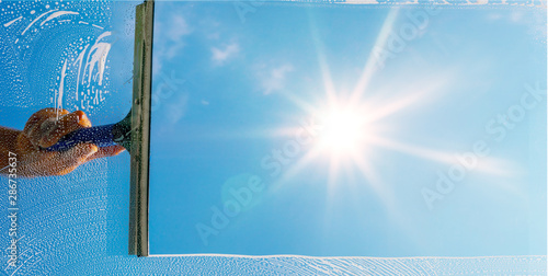 Fensterputzer putzt Fenster mit Schaum und Abzieher im Sonnenlicht - Panorama
