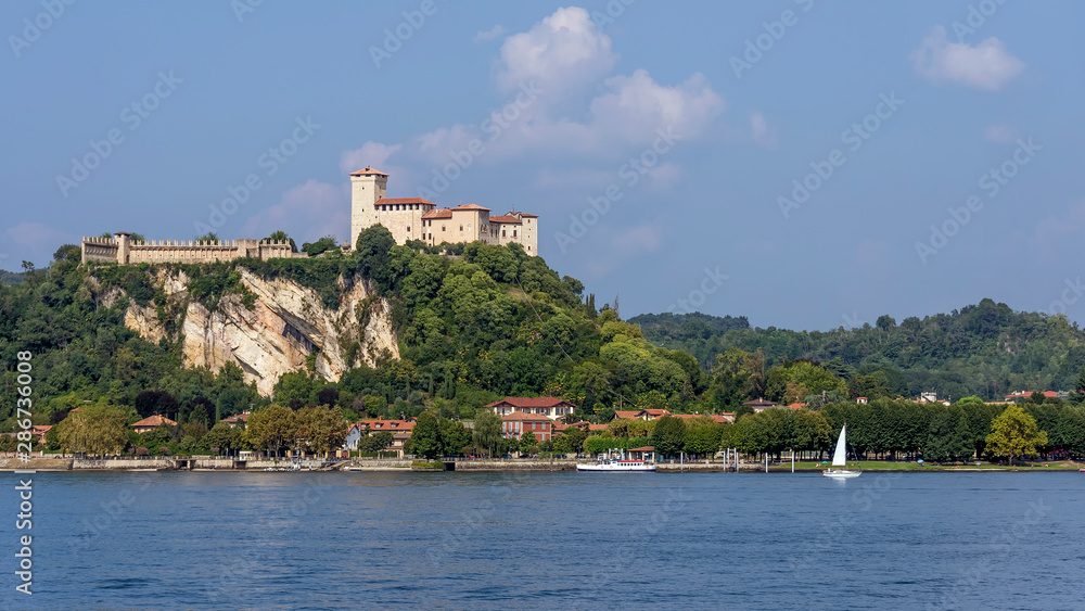 A white sailboat sails on Lake Maggiore near the Rocca di Angera, Varese, Italy