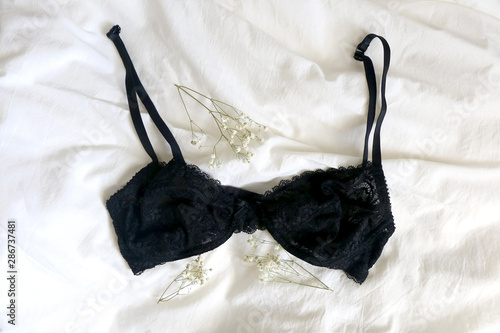 Black lace bralette and gypsophila flowers on white sheets. Top view.