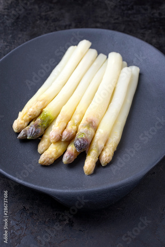 Traditional blanched white asparagus with purple heads as top view on a cast iron design plate with copy space