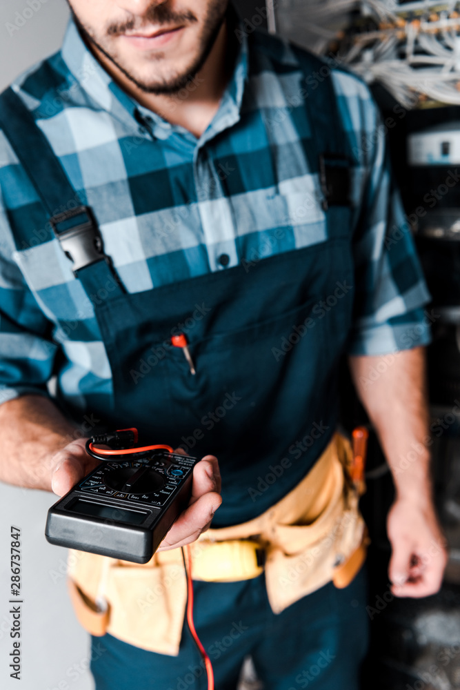 cropped view of bearded technician holding digital meter