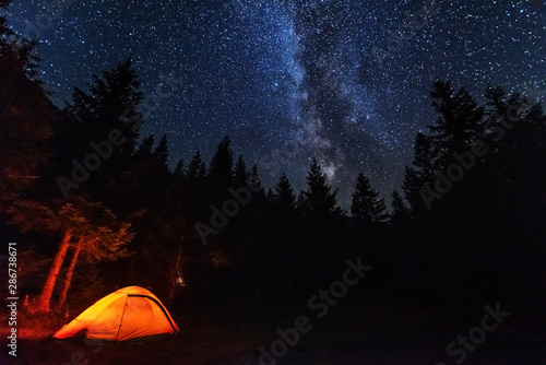 Fantastic starry night with galaxy Milky Way with a tourist and a tent on the mountain range in the Ukrainian Carpathians