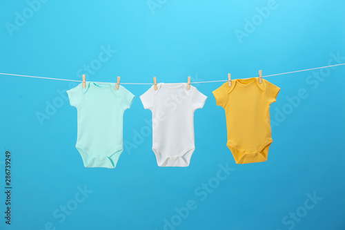 Colorful baby onesies hanging on clothes line against blue background. Laundry day