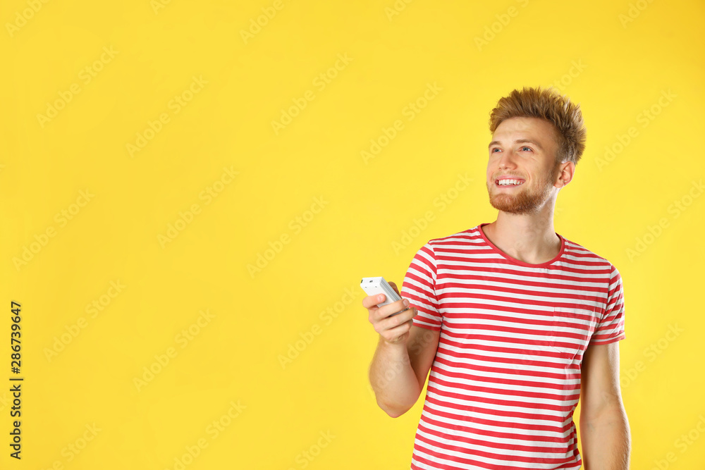 Young man with air conditioner remote on yellow background. Space for text Young man with air conditioner remote on yellow background. Space for text