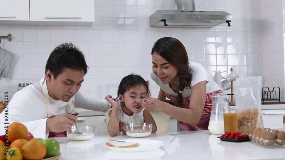 Happy Asian family make a cooking. Father, Mother and Daughter are eating breakfast, cereal with milk in the kitchen at home. Healthy food concept and happy holidays Happy Asian family make a cooking. Father, Mother and Daughter are eating breakfast, cereal with milk in the kitchen at home. Healthy food concept and happy holidays
