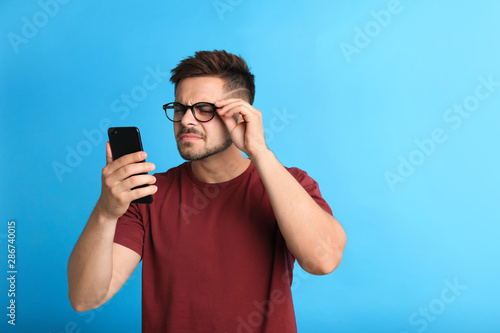 Canvastavla Young man with vision problems using smartphone on blue background, space for te