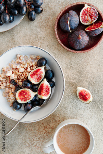 Top view of a breakfast bowl with granola, blue grape and fig slices. Healthy vegan eating flat lay.