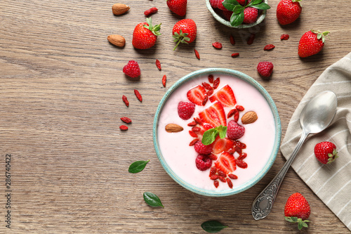 Smoothie bowl with goji berries and spoon on wooden table, flat lay. Space for text