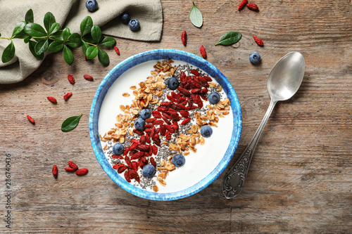 Smoothie bowl with goji berries and spoon on wooden table, flat lay