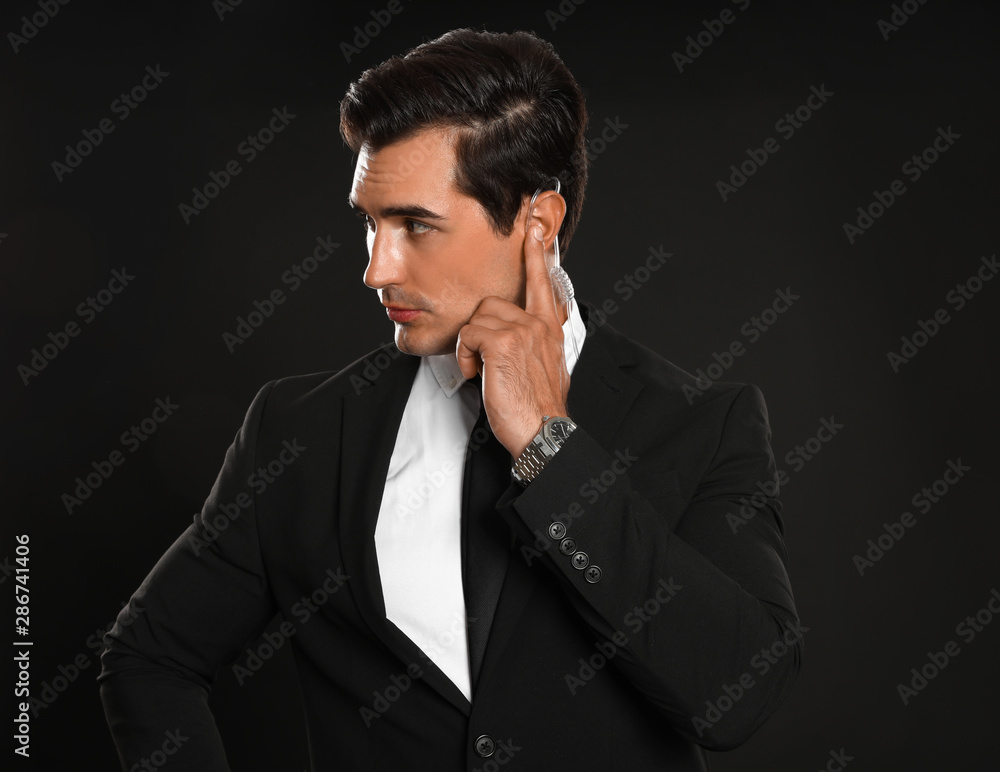 Male security guard in uniform using radio earpiece on dark background Male security guard in uniform using radio earpiece on dark background