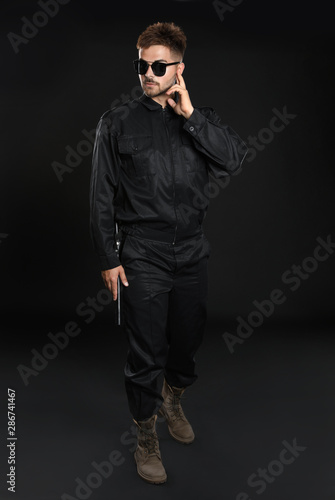 Male security guard in uniform using radio earpiece on dark background