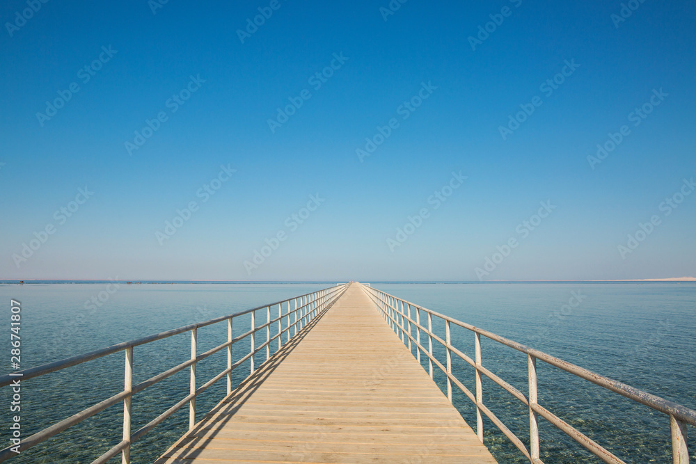 Wooden pier extending into the distance beyond the horizon. Blue sky without clouds. Amazing travel background