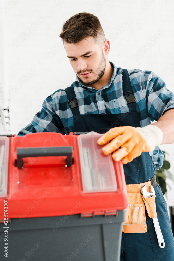 handsome handyman looking at toolbox in kitchen handsome handyman looking at toolbox in kitchen