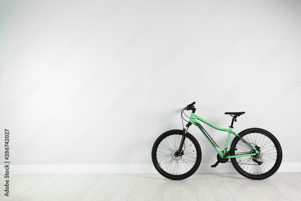 Modern bicycle near white wall indoors. Space for text