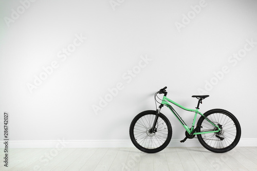 Modern bicycle near white wall indoors. Space for text