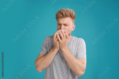 Young man suffering from allergy on blue background
