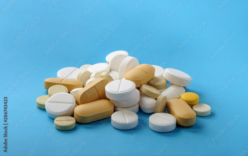 Different tablets and pills on blue background. Top view. Medical and pharmacy concept.