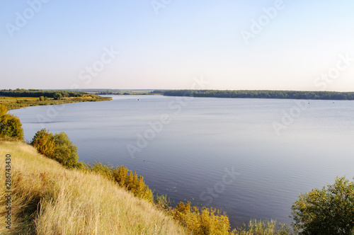 Beautiful natural scenery of a wide river from above in windless sunny autumn day with clear sky. Landscape of shore river reservoir with forest and wetlands. © Nata Studio