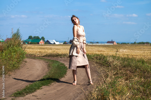 Young beautiful brunette model in a beige dress posing against the background of a mowed wheat field