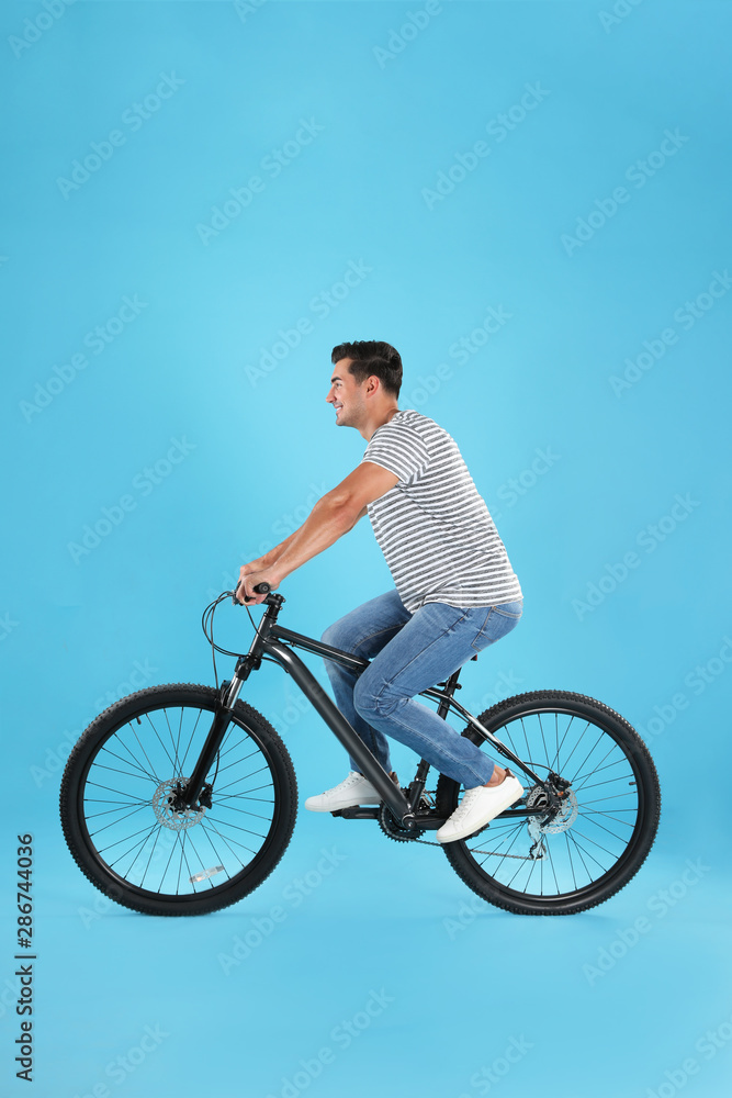 Handsome young man with modern bicycle on light blue background Handsome young man with modern bicycle on light blue background