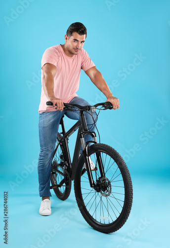 Handsome young man with modern bicycle on light blue background