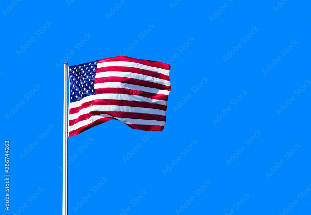 American flag waving proudly on a clear windy day, blue sky background American flag waving proudly on a clear windy day, blue sky background
