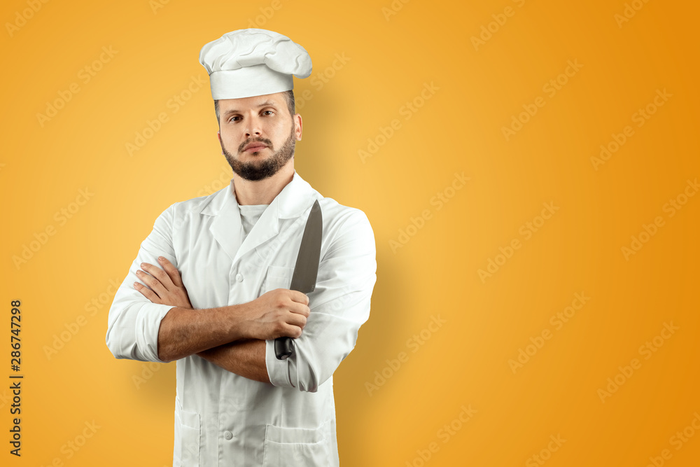 Man with a beard, a cook in a hat and a knife in his hand Isolated on a yellow background. Cooking, recipes, cuisine. Man with a beard, a cook in a hat and a knife in his hand Isolated on a yellow background. Cooking, recipes, cuisine.