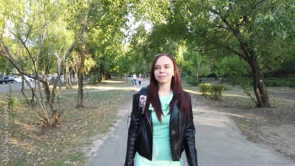 A young woman with natural beauty in a dress and a leather jacket walks through the park. woman with a backpack walking in the Park A young woman with natural beauty in a dress and a leather jacket walks through the park. woman with a backpack walking in the Park