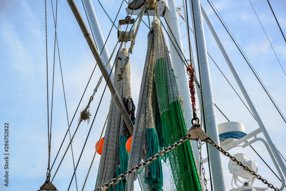 nets and ropes at the cranes of a fishing boat against the blue sky with clouds nets and ropes at the cranes of a fishing boat against the blue sky with clouds