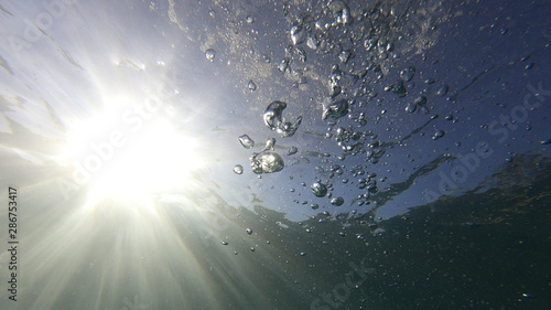 Underwater bubbles with sunlight through water surface as seen in natural scene at Caribbean turquoise open ocean sea
