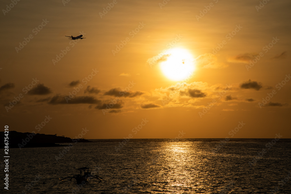 Sunset view of the beach with a plane silhouette taking off
