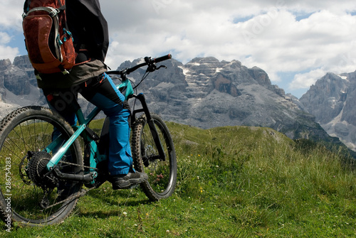 man with electric bike, e-bike, ebike, looking mountains of Tosa and Brenta Peak, Grosté Pass, meadow, Dolomites, Madonna di Campiglio, summer, sport, adventure, travel, Alps, Trentino, Italy