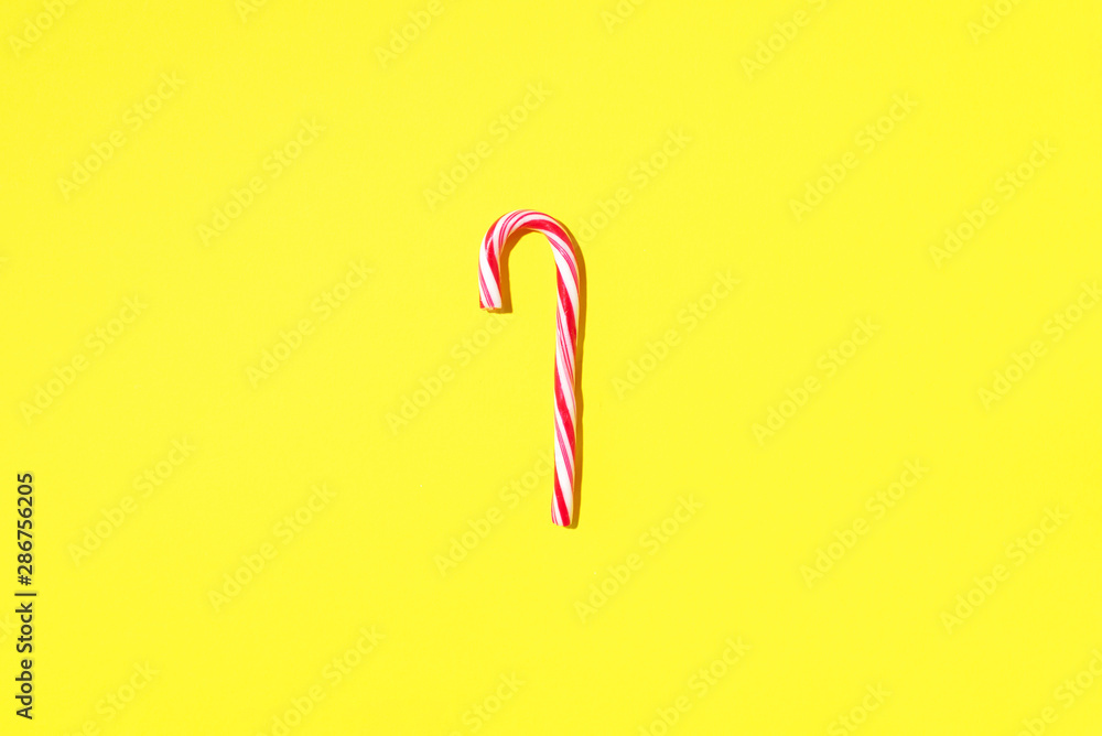 Obraz premium Christmas candy cane on yellow background with copy space. Top view. Greeting card on Christmas and New Year. Minimal festive concept