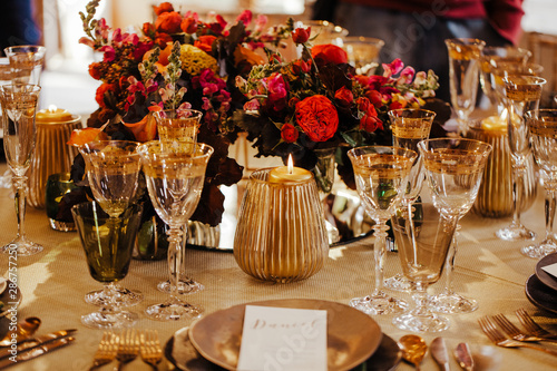 Table set for an event party or wedding reception. Beautiful flowers and glassware set on the table. Selective focus on flowers. Warm colours.