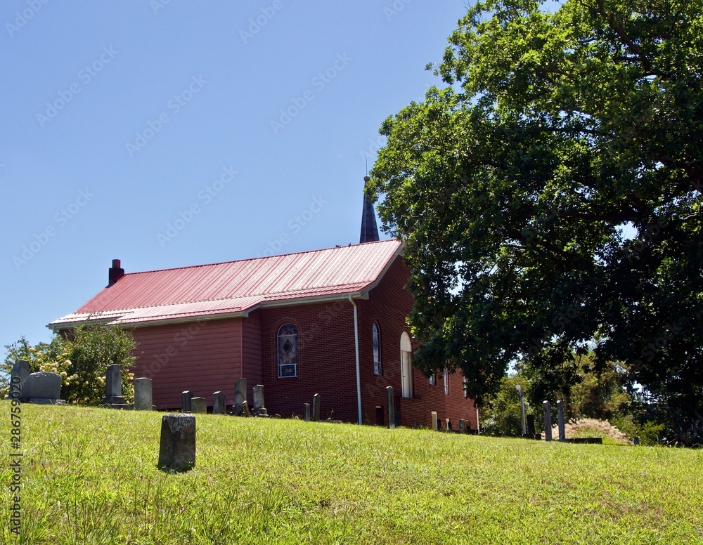 Fototapeta premium Metal Roof, Green Steeple, and Cemetery near a Red Brick Church