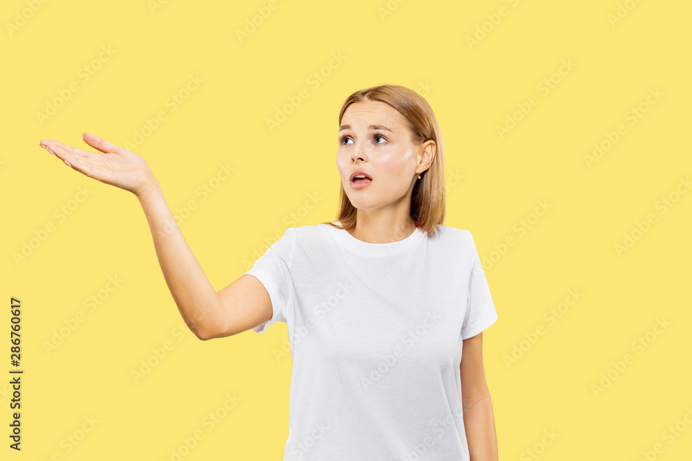 Caucasian young woman's half-length portrait on yellow studio background. Beautiful female model in white shirt. Concept of human emotions, facial expression. Showing an empty space or inviting. Caucasian young woman's half-length portrait on yellow studio background. Beautiful female model in white shirt. Concept of human emotions, facial expression. Showing an empty space or inviting.