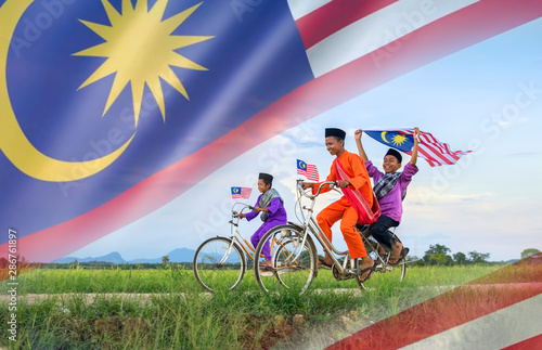 independence Day concept - Two happy young local boy riding old bicycle at paddy field holding a Malaysian flag