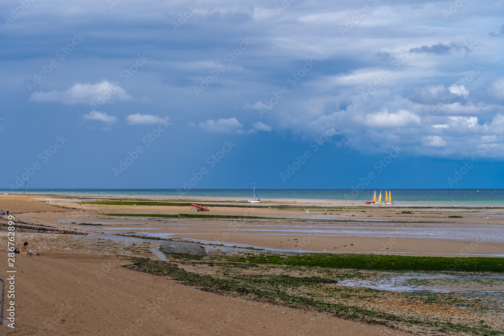 Luc-Sur-Mer, France - 08 12 2019:  View of the beach from with groups of people and sailing boats