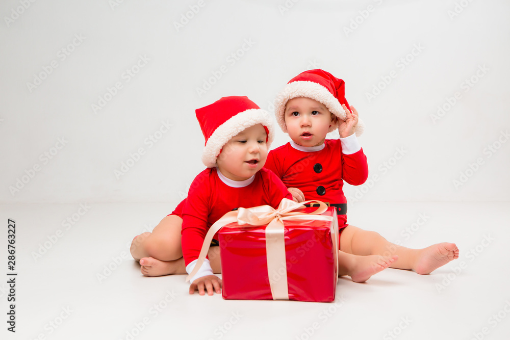 two toddlers in Santa Claus costumes with gift box on white isolate background two toddlers in Santa Claus costumes with gift box on white isolate background