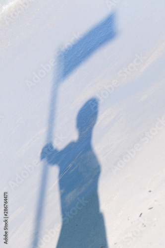 Closeup of a blue shadow of a man holding flag in his hand on the white beach sand background