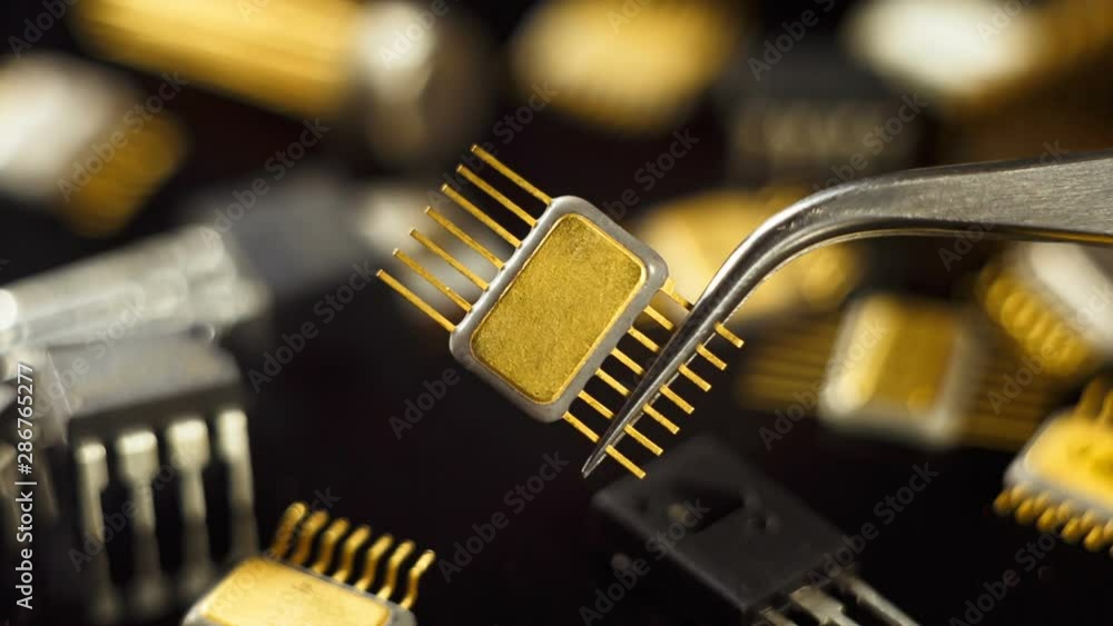 Golden microchip with tweezers on the background of electronic components. Golden microchip with tweezers on the background of electronic components.
