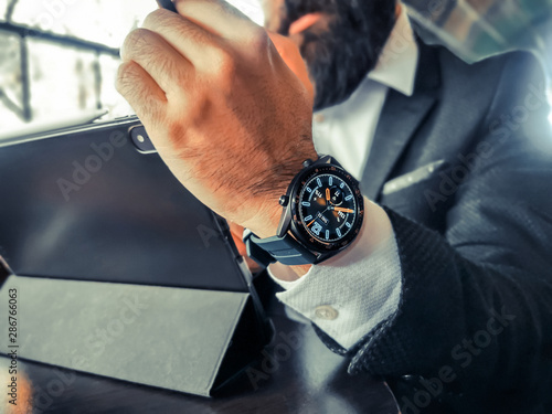 bearded adult rich businessman who has smart watch using his pro tablet and work remotely