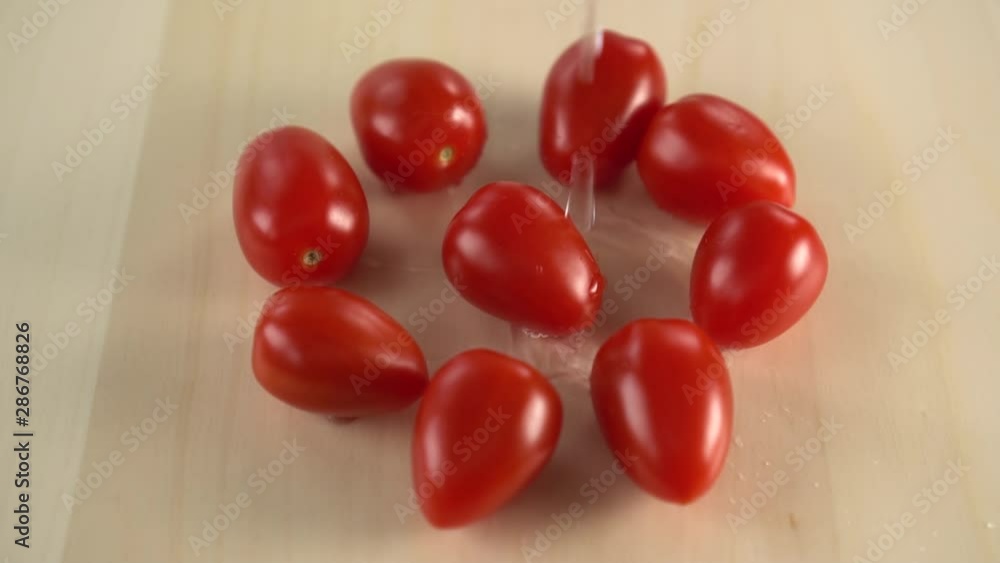 Several red juicy cherry tomatoes are spinning on a wooden surface. A stream of water for washing drops from above. Cooking vegan dishes Several red juicy cherry tomatoes are spinning on a wooden surface. A stream of water for washing drops from above. Cooking vegan dishes